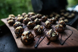Wooden board with stuffed mushrooms drizzled with a dark sauce on a blurred background