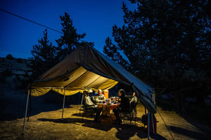 People sitting at a table under a large tent in a forest at night.