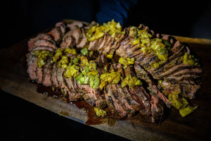 Sliced beef with green herb garnish on a wooden board against a dark background