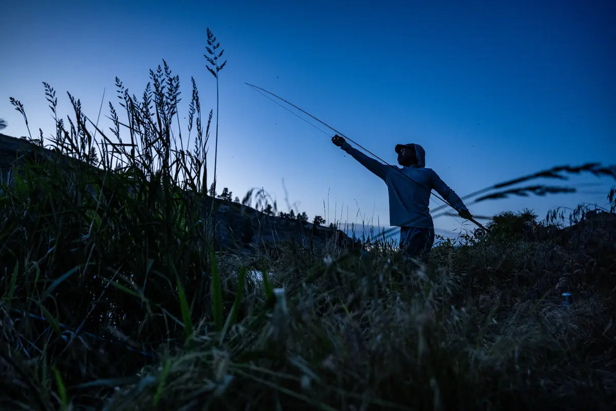 Person fishing at dusk with tall grass and a blue sky in the background